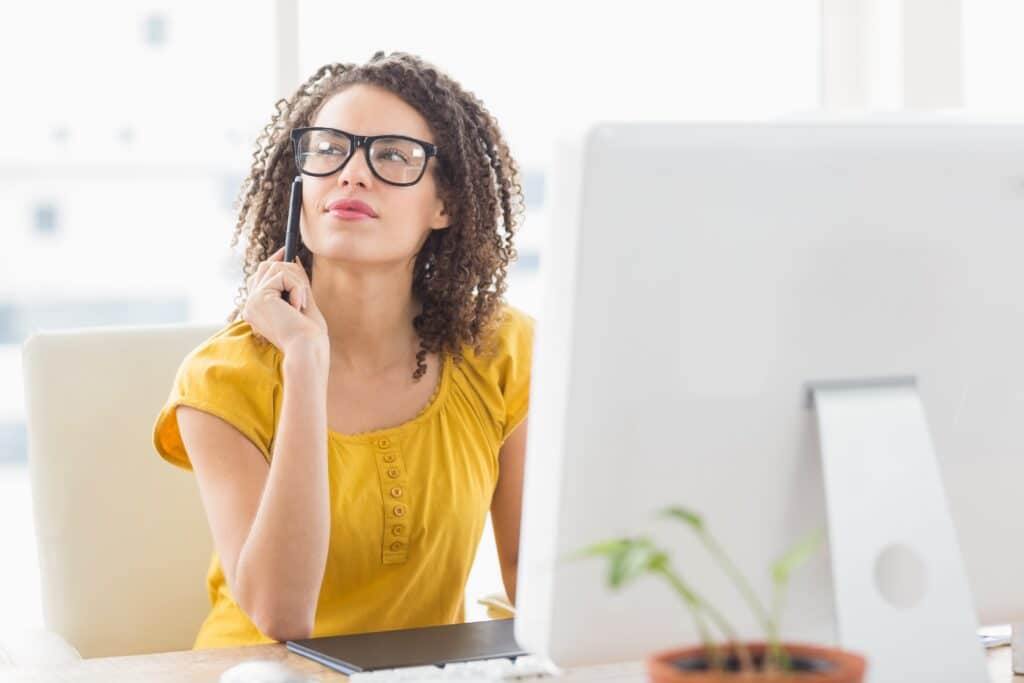 Young woman wearing glasses, thinking in front of computer